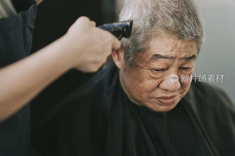 an asian chinese mid adult woman is cutting and trimming hair for her father in the kitchen due to travel ban